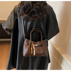 Détail d'un sac seau en cuir grainé marron foncé avec fermoir rotatif et breloque en perles