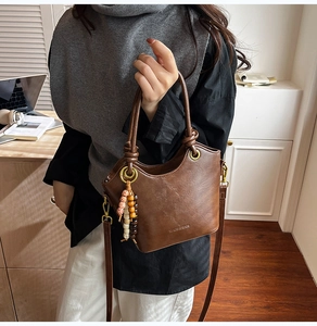 Detail of soft brown leather bucket bag with wooden bead charm on office desk background
