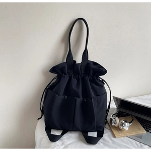 Detail of minimalist black canvas bucket bag with drawstring closure and large front pockets