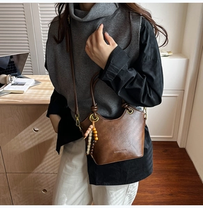 Detail of dark brown retro bucket bag with wooden bead charm and long shoulder strap