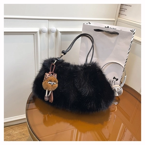 Close-up of black fuzzy plush shoulder bag with brown faux fur doll pendant on a table