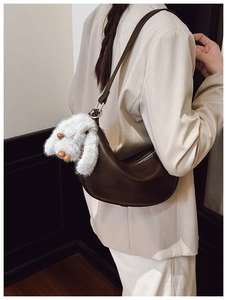 Detail of dark coffee leather croissant bag with white plush rabbit charm on strap