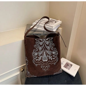 Detailaufnahme der ethnischen weißen Stickerei auf einer dunkelbraunen Wildledertasche