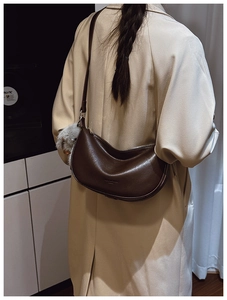 Detail of a dark brown half-moon underarm bag with a plush doll charm on a leather strap