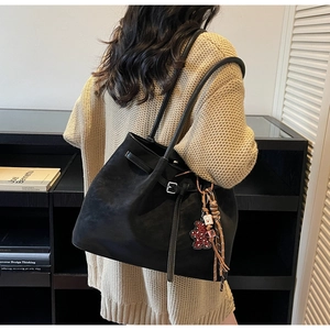 Detail view of a large black suede tote bag featuring a heart bear charm and fringe