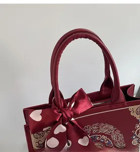 Close-up of red wedding handbag with golden dragon-phoenix embroidery and silk bow