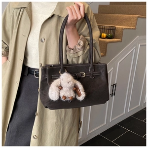 Detail of dark brown leather tote with metal turn-lock and white fluffy rabbit charm