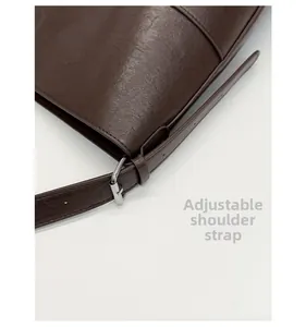 Détail de la bandoulière réglable avec boucle argentée sur sac seau en cuir grainé marron