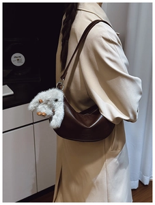 Brown half-moon underarm bag with cute plush bunny charm shown in lifestyle shot