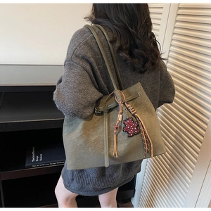 Detail view of olive green leather tote bag with buckle strap and leopard bear charm