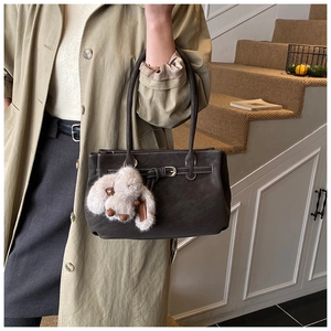 Detail of dark brown leather tote bag with white stitching and plush bunny pendant