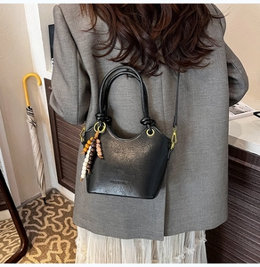 Detail of black soft leather bucket bag with gold hardware and wooden bead pendant accessory