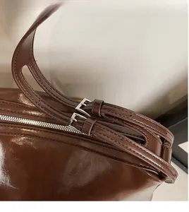 Detail of dark brown glossy leather shoulder bag with adjustable silver buckle straps