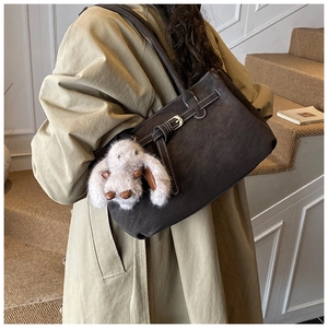 Close-up of dark coffee leather tote bag with a plush bunny charm and gold metal buckle