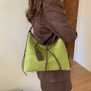 Detail of green suede shoulder bag featuring long fringe tassels and brown leather trim