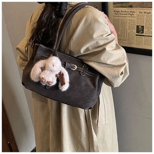 Detail of dark brown tote bag with metal buckle and plush rabbit charm on trench coat