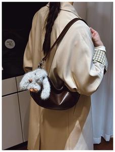 Detail of dark brown leather half-moon bag with cute gray bunny plush keychain on a model