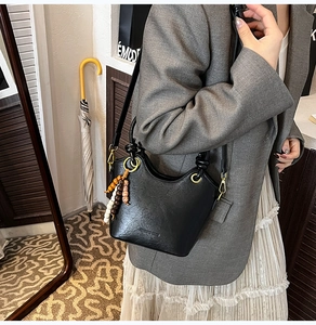 Close-up of black leather bucket bag with retro beaded charm and embossed logo detail