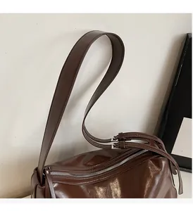 Detail of dark brown glossy leather tote bag showing wide strap and silver metal buckle