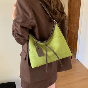 Close-up of green matte suede shoulder bag with brown leather trim on model