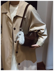 Detail of dark brown crescent shoulder bag with a plush rabbit charm on a model