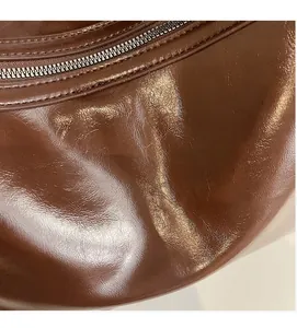 Detailed macro view of the glossy dark brown leather texture and metal zipper closure