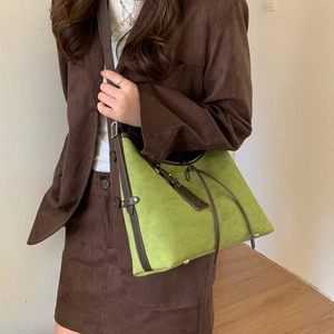 Detail of green suede tote bag with brown leather trim and metal base studs