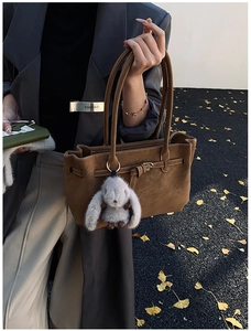 Close-up of brown suede tote bag with metal buckle strap and plush rabbit charm