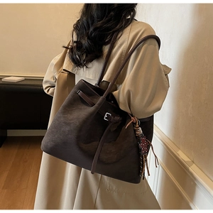Detail of dark brown suede tote bag featuring a leather strap buckle and woven pendant