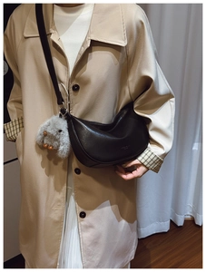 Detail of black leather crescent bag with cute plush rabbit charm on beige trench coat