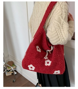 Close-up of red knit tote bag featuring white floral embroidery and drawstring closure