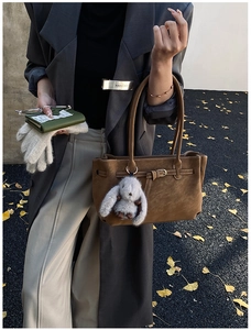 Detail of brown faux suede tote bag featuring a decorative belt and plush bunny keychain