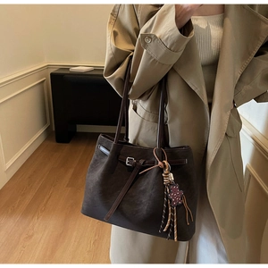 Detail view of large dark brown tote bag with suede texture and woven tassel charm
