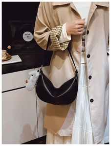 Detail view of a black crescent hobo bag with a plush bear charm on a trench coat model