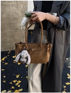 Brown leather tote bag with retro buckle and grey rabbit plush pendant in autumn setting