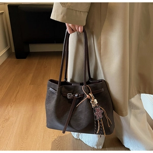 Detail of dark brown tote bag with bear charm pendant and leather strap closure
