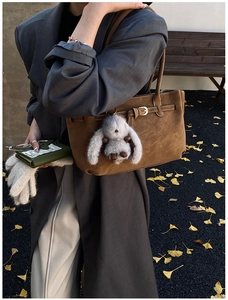 Brown suede tote bag with plush rabbit charm and green wallet on autumn ginkgo leaves