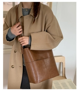 Détail d'un sac seau en cuir marron avec poche extérieure porté en bandoulière par un modèle