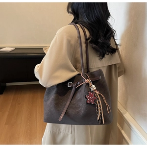 Detail of dark brown suede tote bag with leopard bear charm and tassel on beige coat