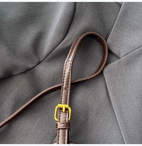 Close-up of dark brown leather shoulder strap with gold buckle and stitching details