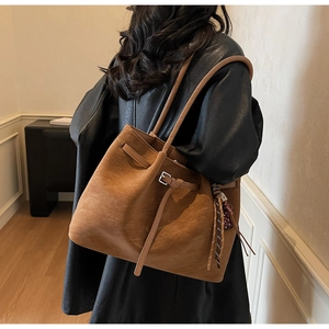Detail of a brown suede tote bag with metal buckle and woven tassel decoration