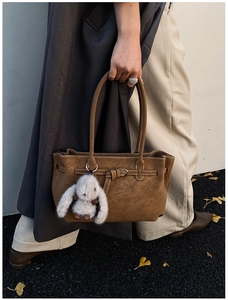 Detail of brown suede tote bag with contrast stitching and a plush bunny charm on a street