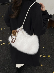 White faux fur hobo bag with braided strap and plush ball charm in autumn outdoor setting