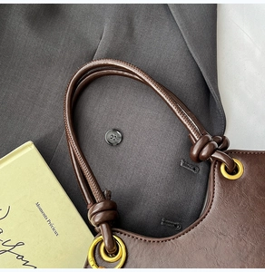 Close-up of soft leather bucket bag with golden metal rings and decorative knot handle