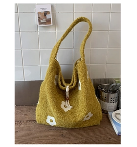 Detail of yellow plush tote bag showing knit texture with white floral embroidery and tassels