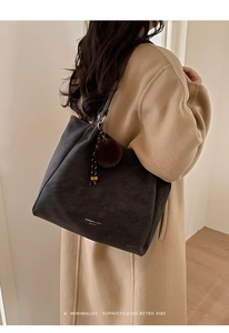 Detailed view of grey leather tote bag with plush charm on a model in wool coat