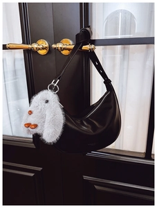 Close-up of black leather hobo bag with plush rabbit charm on a black wooden door