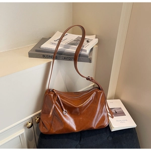 Detail of a brown glossy leather tote bag showing adjustable strap and metal zipper