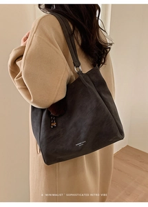 Detail of a large black leather tote bag with brand logo and plush charm accessory
