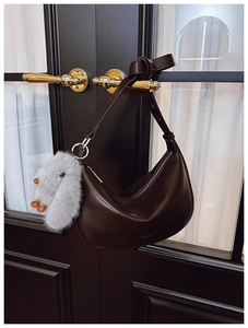 Detail of dark brown leather crescent bag with plush rabbit charm on a vintage door